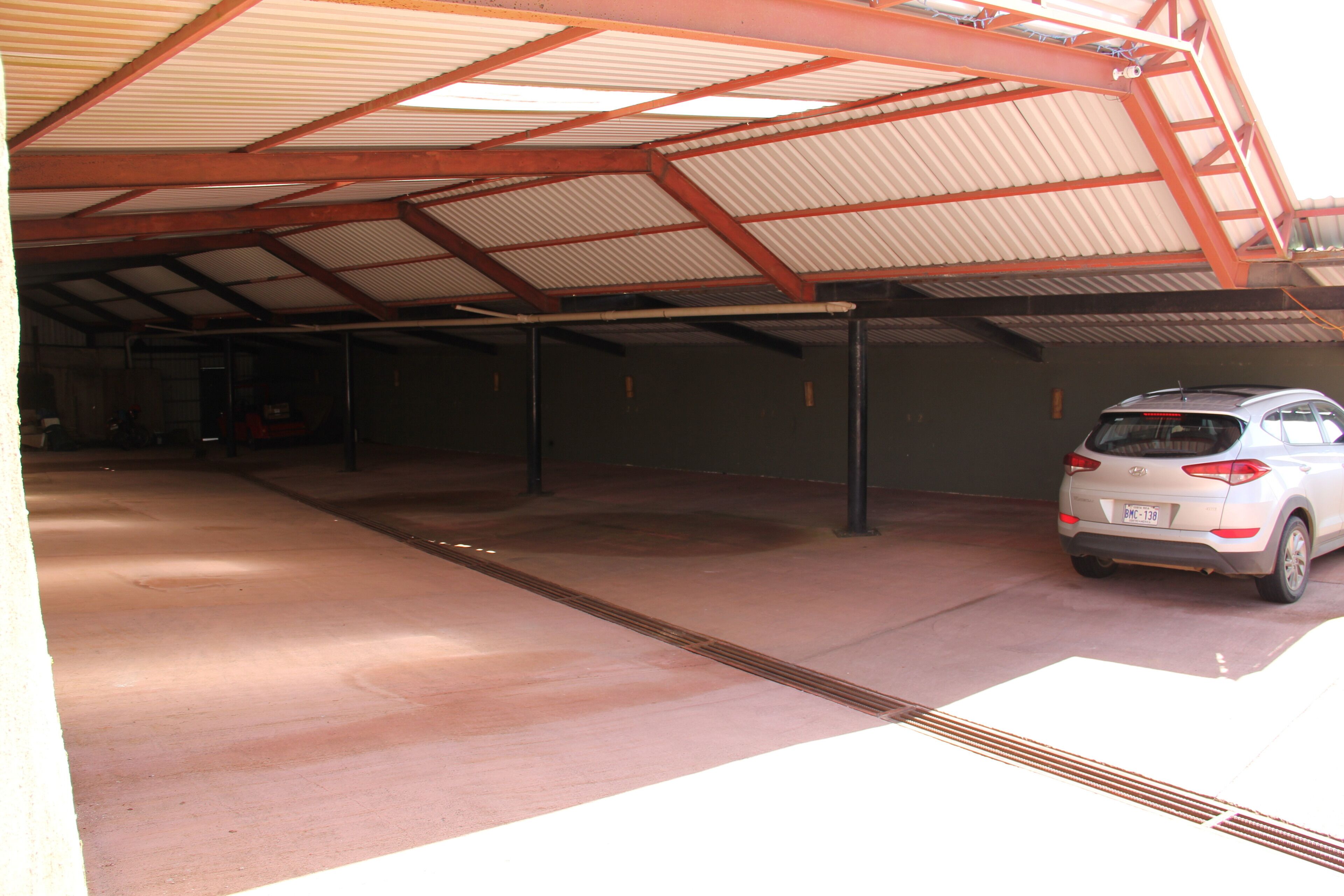 Un espace de stationnement couvert où est garée une voiture blanche.