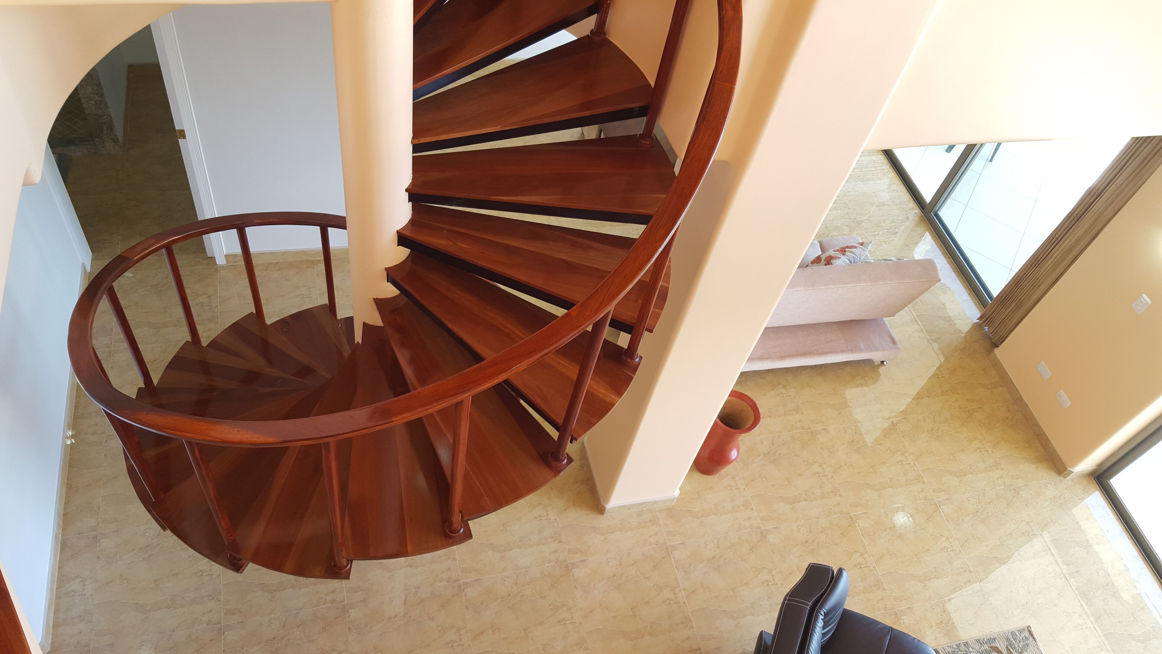A wooden spiral staircase in a room with a tiled floor and a sofa.
