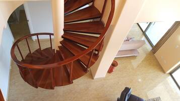 A wooden spiral staircase in a room with a tiled floor and a sofa.
