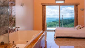 Une salle de bain dotée d’une grande baignoire, d’un miroir et offrant une vue sur un paysage montagneux par la fenêtre.