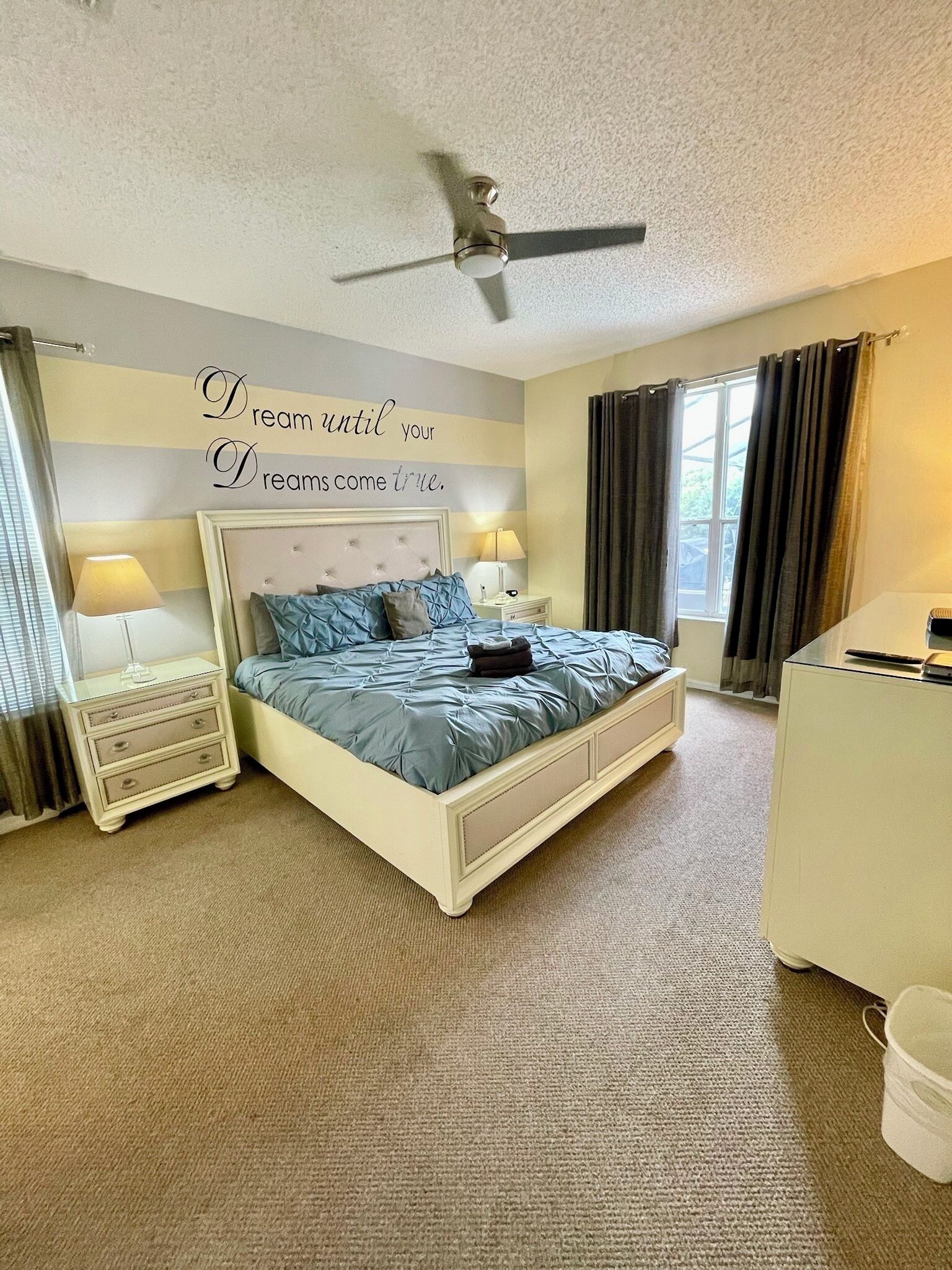 A bedroom with a bed, bedside tables, a ceiling fan, and a window with curtains.