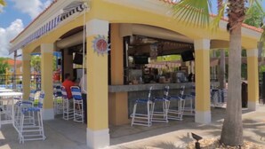 A covered outdoor seating area with a bar, white metal chairs, and a palm tree. - 7 BDRM, Private Pool/HotTub, Heat Included, Games (Kissimmee)