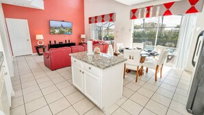 A modern kitchen with a central island, a dining area with a glass table, and a living area with a red sofa. - 7 BDRM, Private Pool/HotTub, Heat Included, Games (Kissimmee)