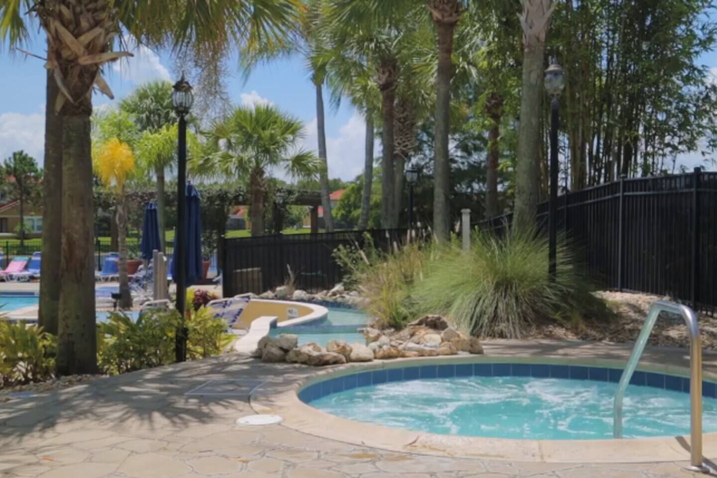 A pool area with a hot tub, lounge chairs, and palm trees.