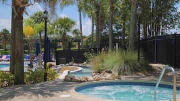 A pool area with a hot tub, lounge chairs, and palm trees.