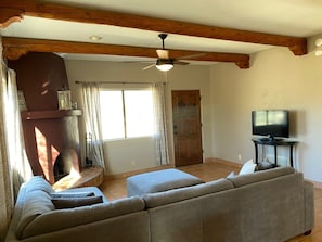 A living room with a fireplace, a ceiling fan, a television on a stand, and a large window with curtains.