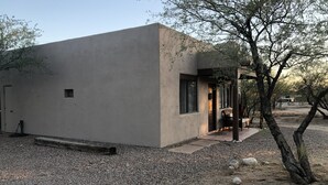A modern building with a concrete exterior, a small porch, and a gravel driveway. - Ranch Casita: views, views, views! (Tucson)