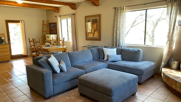 A living room with a sectional sofa, a dining area with a table and chairs, and a large window with curtains. - Ranch Casita: views, views, views! (Tucson)