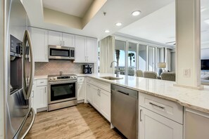 A modern kitchen with stainless steel appliances, white cabinetry, and a view of the outdoors.