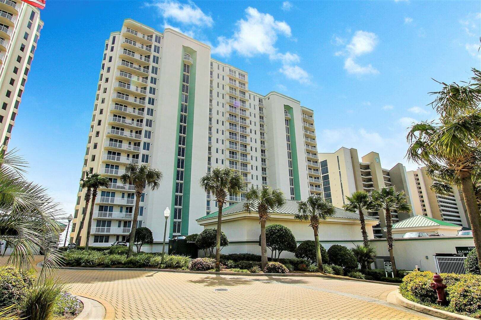 A high-rise hotel with multiple floors, a central green vertical feature, and a landscaped courtyard with palm trees.