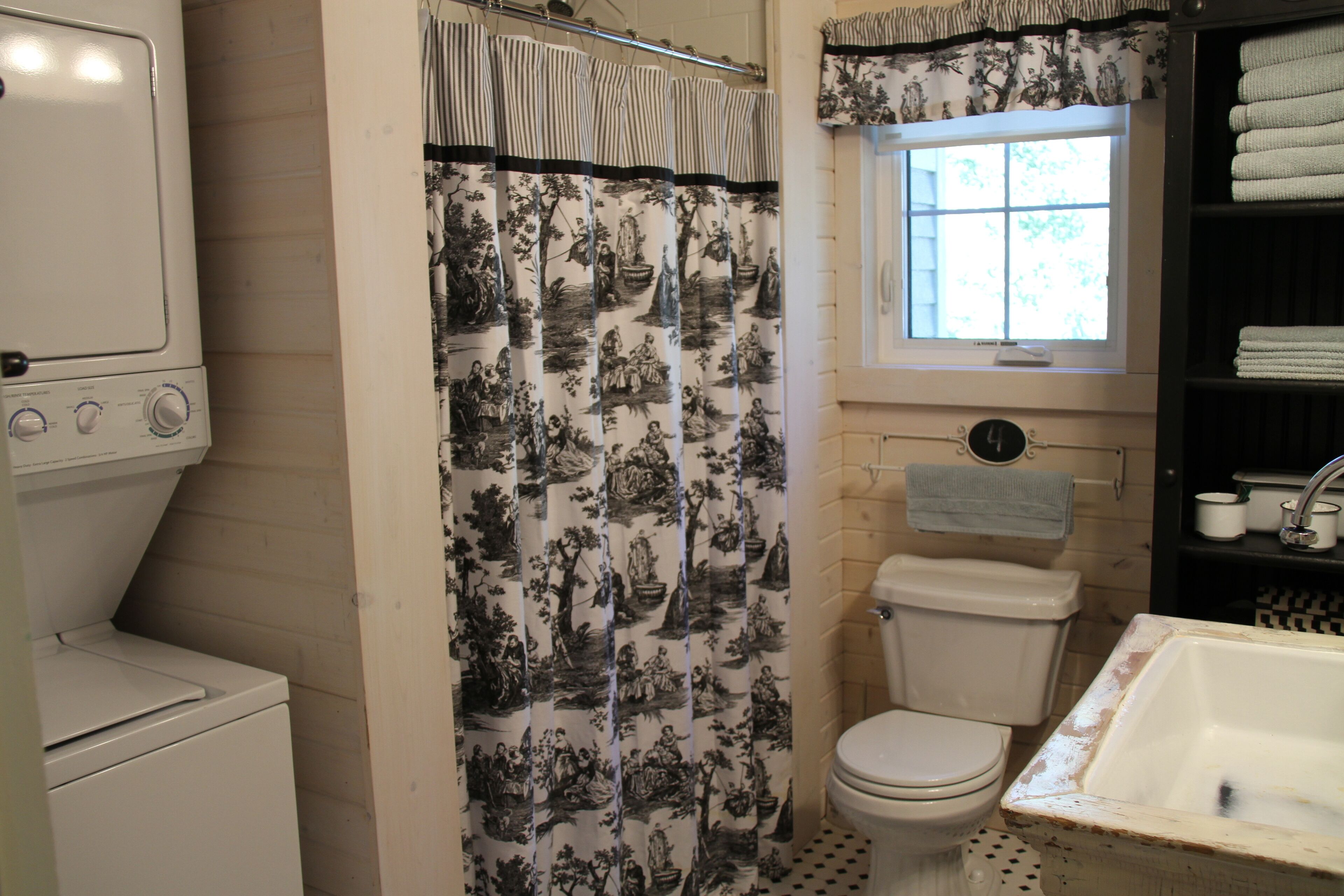 Ein Badezimmer mit Toilette, Waschbecken, einer Duschkabine mit Blumenmuster und einem Fenster mit Blick auf Bäume.
