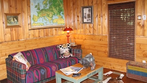 Ein gemütliches Blockhaus-Interieur mit einer Karo-Couch, einer Karte an der Wand und einer Bärenstatue auf einem Tisch.