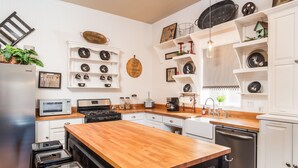 A modern kitchen with white cabinetry, a wooden island, and various decorative items on the walls. - Spacious in & outdoor Gastehaus.Great for enjoying the hill country.Walk to Main (Fredericksburg)