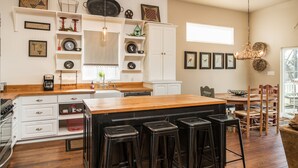 A modern kitchen with a central island, bar stools, and a dining area with a wooden table and chairs. - Spacious in & outdoor Gastehaus.Great for enjoying the hill country.Walk to Main (Fredericksburg)