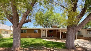 A single-story house with a front porch, a small lawn, and two large trees. - Remodeled in-town beauty with Mountain Views! Large, fully fenced back yard. (Kanab)
