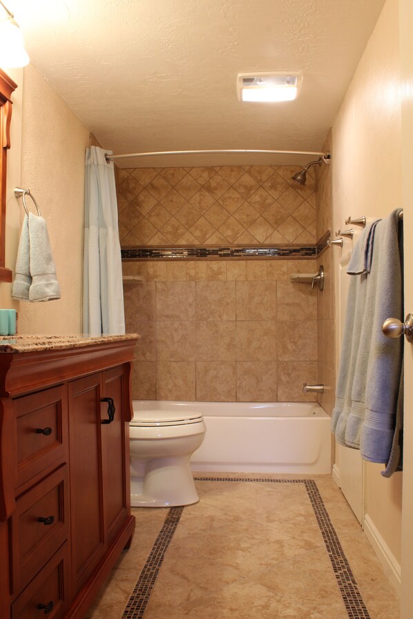 A bathroom with a toilet, bathtub, shower, and wooden vanity.