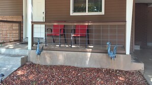 A porch with a railing, a door, and two red chairs. - Remodeled in-town beauty with Mountain Views! Large, fully fenced back yard. (Kanab)