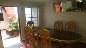 A dining area with a round table and four wooden chairs. There is a window with a view of a red building outside. - New Day House in Cusco (Centro Histórico)