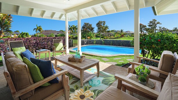 Eine überdachte Terrasse mit Gartenmöbeln, einem Pool und Blick auf eine Wohngegend.