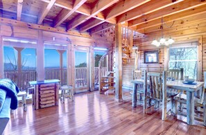 L’intérieur d’un chalet en bois rustique, avec un coin repas, un escalier en bois et de grandes fenêtres.
