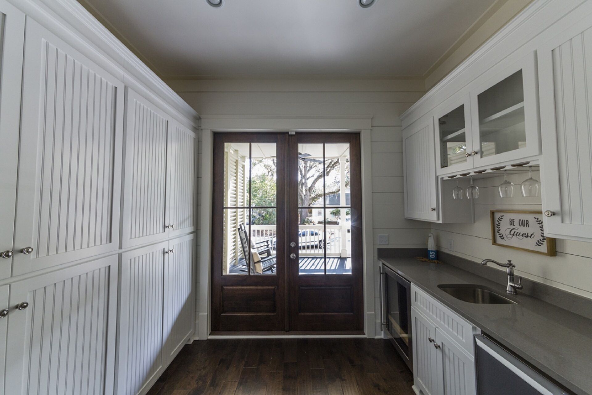 Une cuisine avec des meubles blancs, une porte en bois et une vue sur l’extérieur.