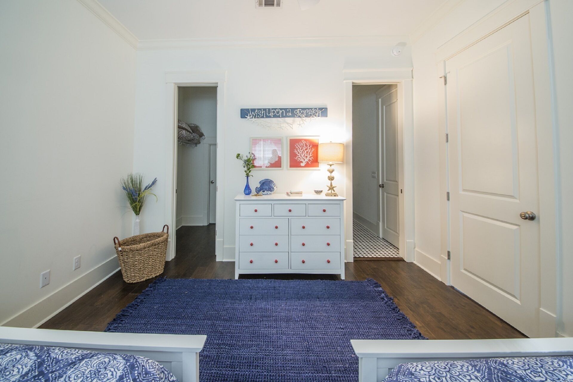 Un couloir avec un tapis bleu, une commode blanche dotée de boutons rouges, et une enseigne au-dessus.