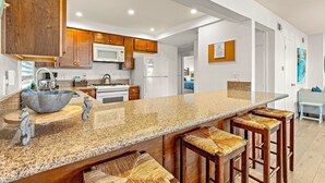 Eine Küche mit Granit-Arbeitsplatten, Holzschränken, einer Edelstahlspüle und einer großen Kochinsel mit Barhocker.