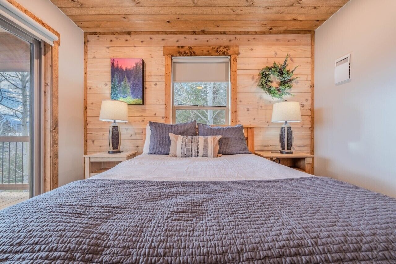Un dormitorio con una cama grande, dos mesitas de noche con lámparas, una ventana con vistas y un cuadro en la pared.
