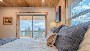 A bedroom with a large bed, a balcony, a chair, and a painting on the wall.