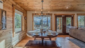 A wooden interior with a dining table set for four, large windows, and a view of the outdoors.
