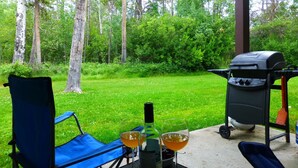 Une terrasse avec un barbecue, deux verres de vin et une bouteille posée sur une table.