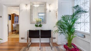Un interior moderno con una mesa consola de vidrio, dos sillas negras, un espejo grande y una planta en maceta.