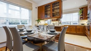 Una cocina moderna con armarios de madera, una mesa de comedor para seis personas y ventanas grandes que dejan entrar luz natural.