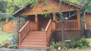 A wooden cabin with a porch, steps, and a small garden area with various plants.
