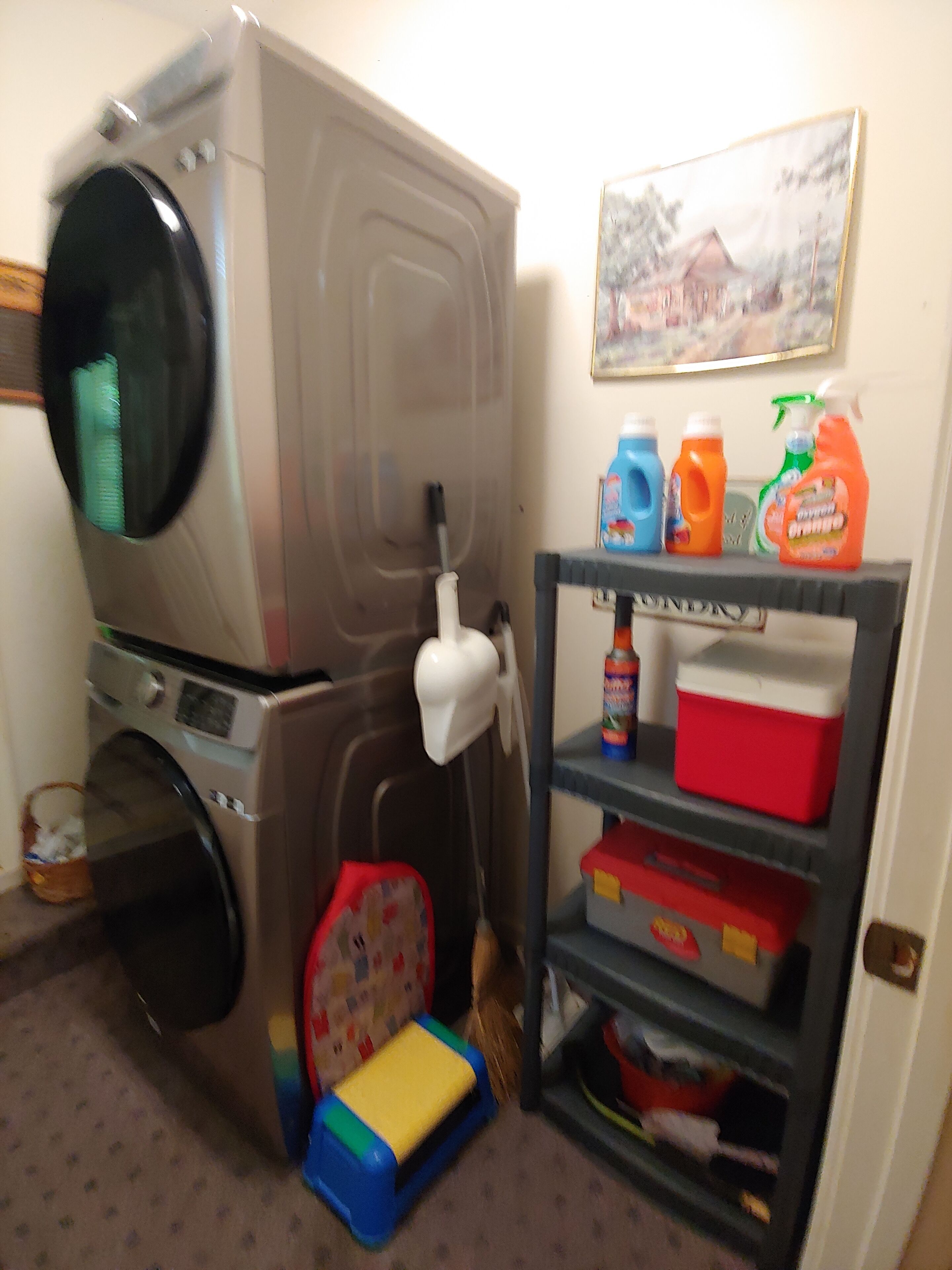 A laundry area with a washing machine, a drying rack, and a shelf with cleaning supplies.