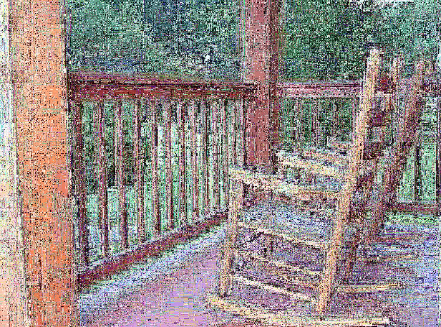 A room with a wooden staircase, a wooden railing, and a view of greenery outside.