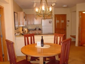 A dining area with a round wooden table and four chairs, a chandelier above, and wooden cabinets in the background.
