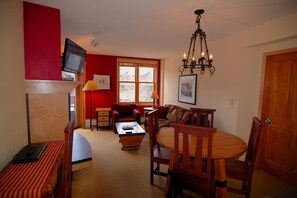 A cozy living room with a red accent wall, a television, a chandelier, a dining table with chairs, and a sofa.