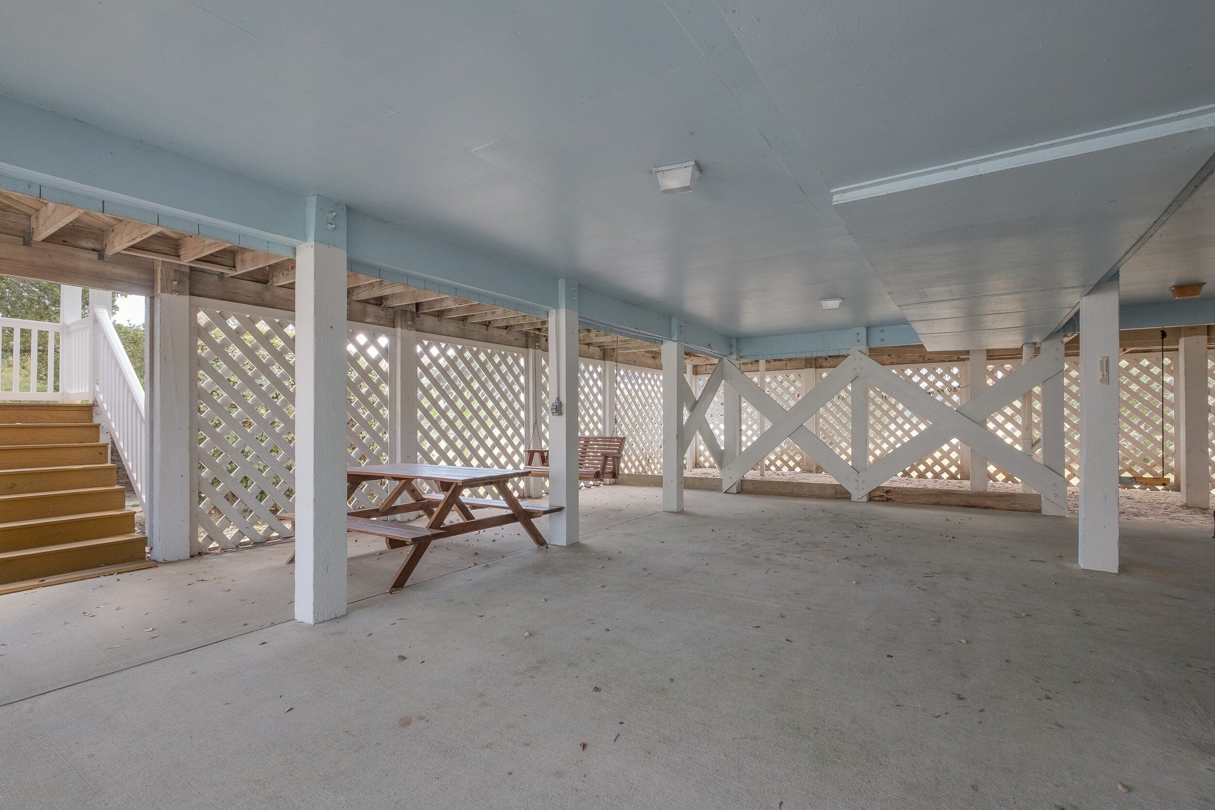 En åben patio med en trætrap, picnicborde og et espalier.