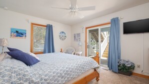 Un dormitorio con cama, ventilador de techo, televisor y vistas al exterior.