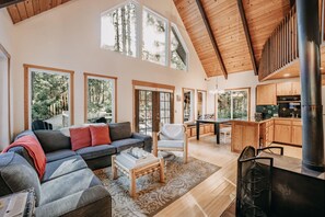 Relax in this spacious living area with a high ceiling and large windows offering a view of the surrounding forest.