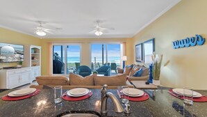 A modern kitchen with a large island, a dining area with a view of the ocean, and a living area with a large window. - Seagull-Gulf Front Home with Private Beach Crossover No Pets (Navarre)