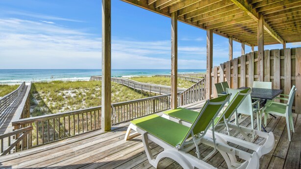 A wooden deck with a view of the beach and ocean, featuring green lounge chairs and a table. - Seagull-Gulf Front Home with Private Beach Crossover No Pets (Navarre)