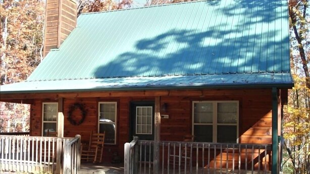 A wooden cabin with a green metal roof, a porch with a railing, and a number '1802' on the door. - Get Away from it All in This Immaculate Cabin in the Woods (Blairsville)