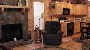 A cozy living room with a fireplace, a stone accent wall, and a comfortable armchair. - Get Away from it All in This Immaculate Cabin in the Woods (Blairsville)