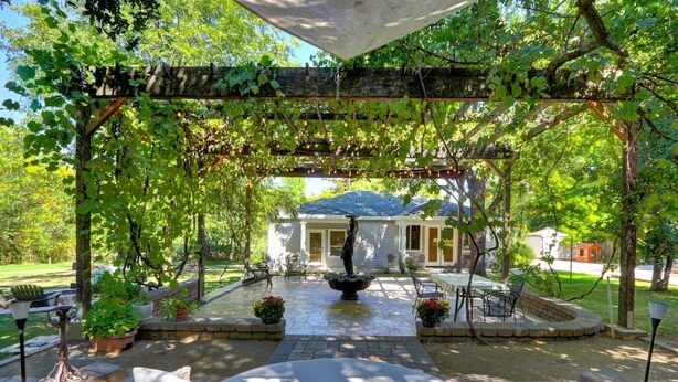 Un patio couvert comprenant un banc en pierre, une fontaine et une pergola recouverte de plantes grimpantes.