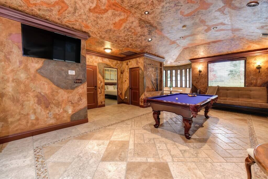 Una habitación amplia con mesa de billar, un sofá y una televisión instalada en la pared.