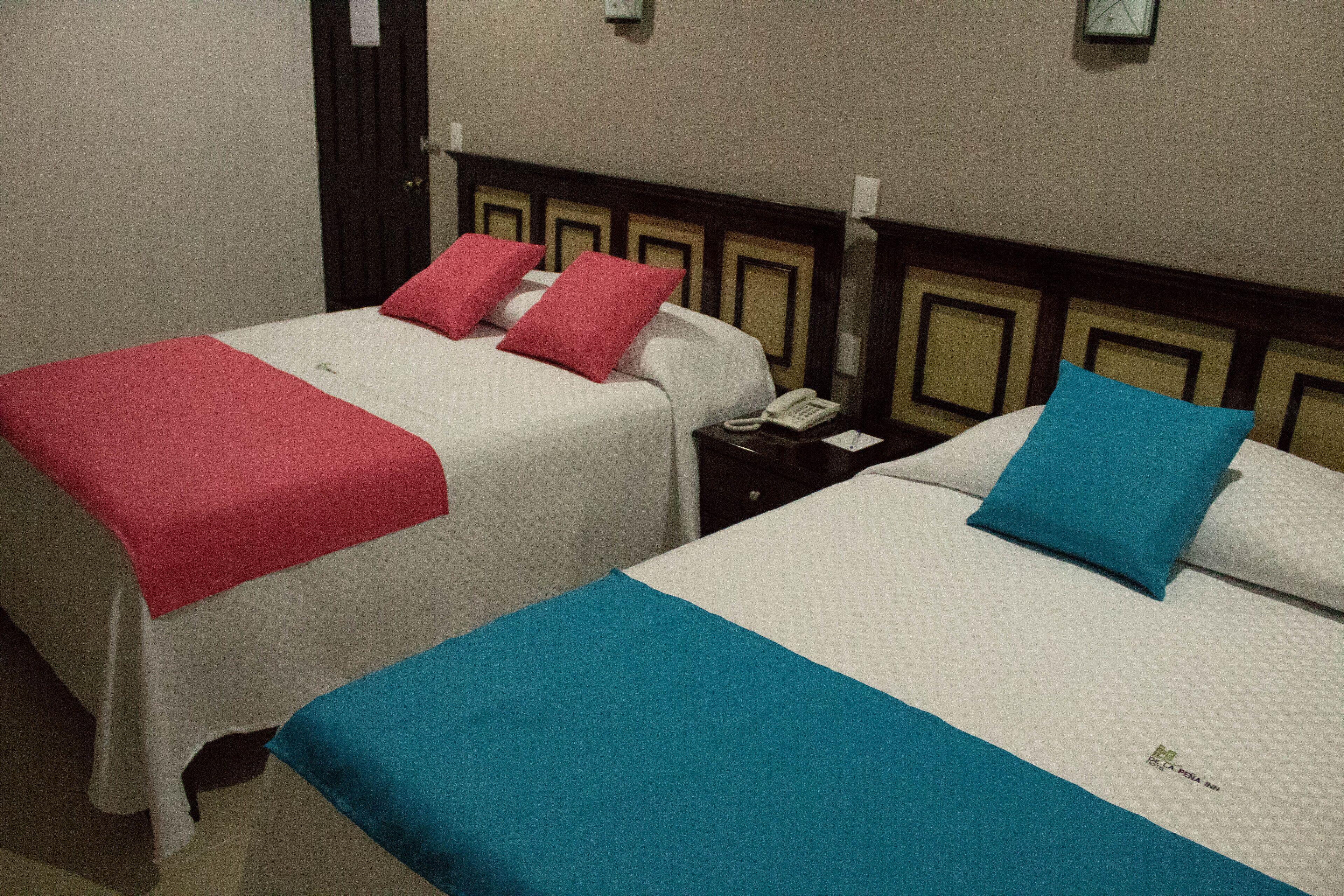 Two twin beds with red and blue bedding, a bedside telephone, and a wall clock.