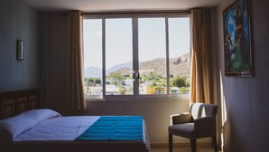 Une chambre d’hôtel avec une grande fenêtre, un lit, une chaise et un tableau au mur.