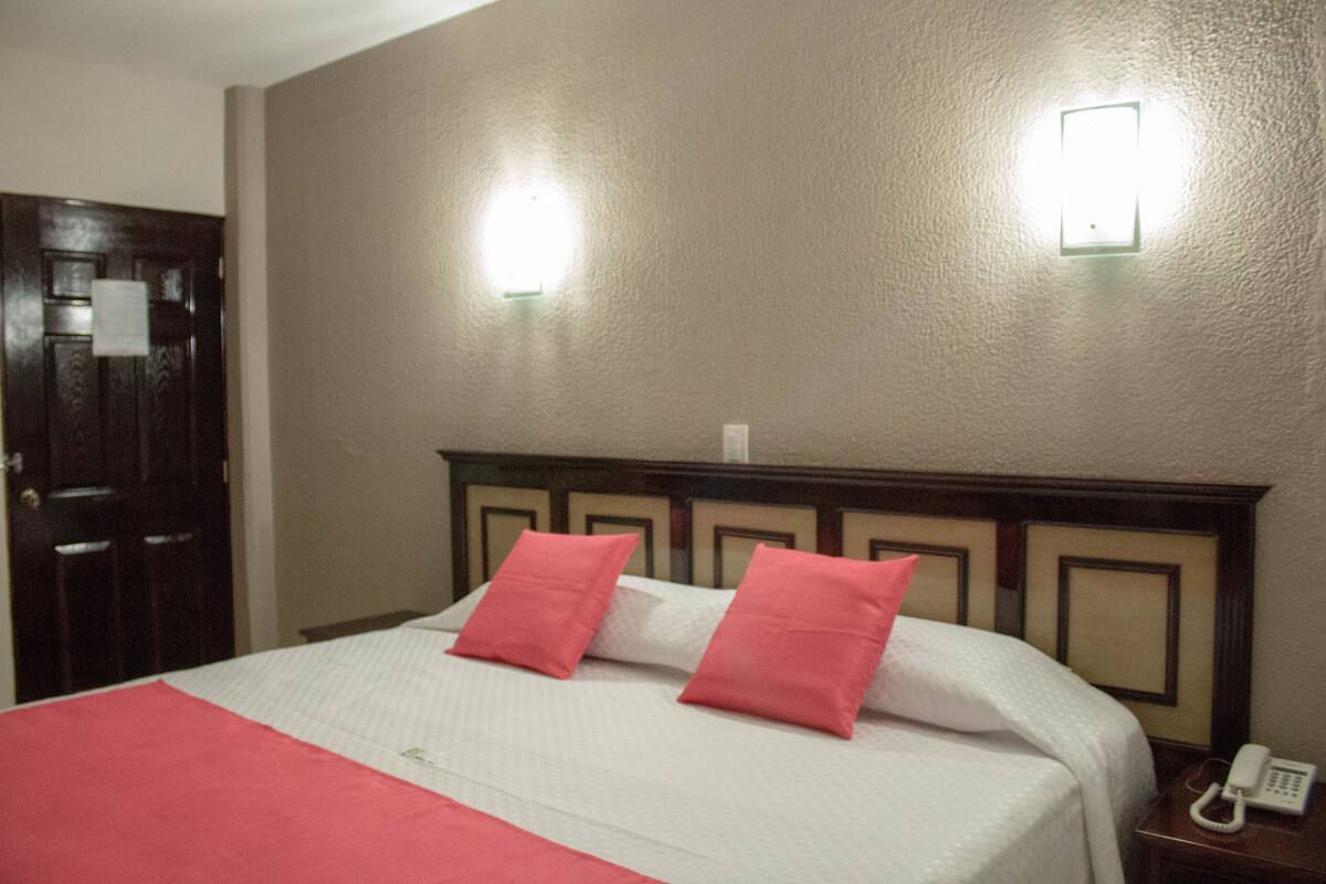 A hotel room with a bed, two pillows, a bedside phone, and two wall-mounted lights.